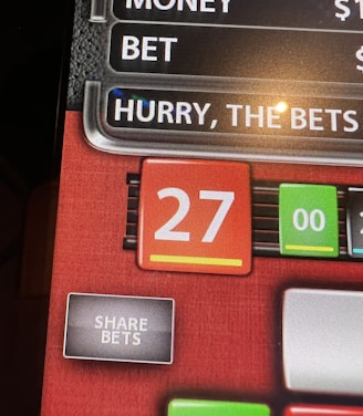 A digital display screen showing a casino betting interface, with text prompting to hurry bets and a highlighted number 27 in red. There are options for betting amounts and a 'share bets' button.